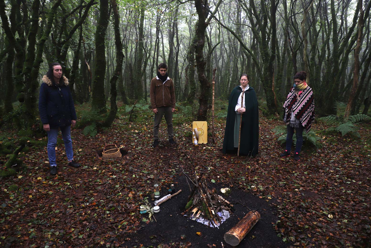 Saison sombre : nous voyons 4 personnes dont un sacerdote dans les bois en cercle autour d’un foyer dont le feu n’est pas encore allumé.